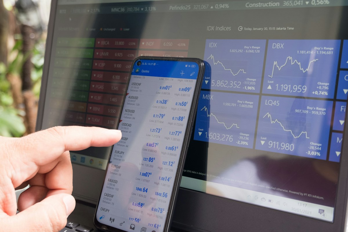 A trader reviewing currency quotes on a smartphone beside a laptop